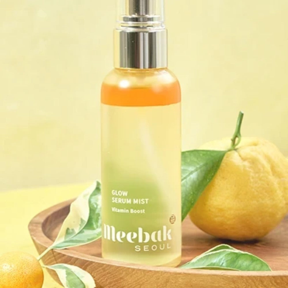Skin TOGO Meebak Glow Serum Mist Vitamin Boost in a clear spray bottle with citrus fruit on a wooden tray