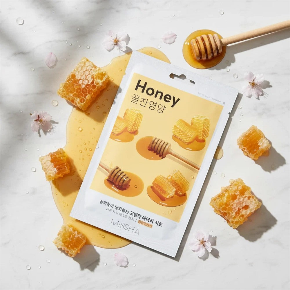 Skin TOGO Missha Airy Fit Honey sheet mask with honeycomb and honey dipper on a marble surface with cherry blossoms.