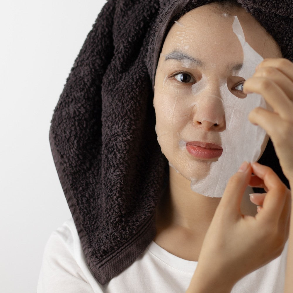 Skin TOGO model applying a moisturizing sheet mask with lotus extract and hyaluronic acid for deep skin hydration.