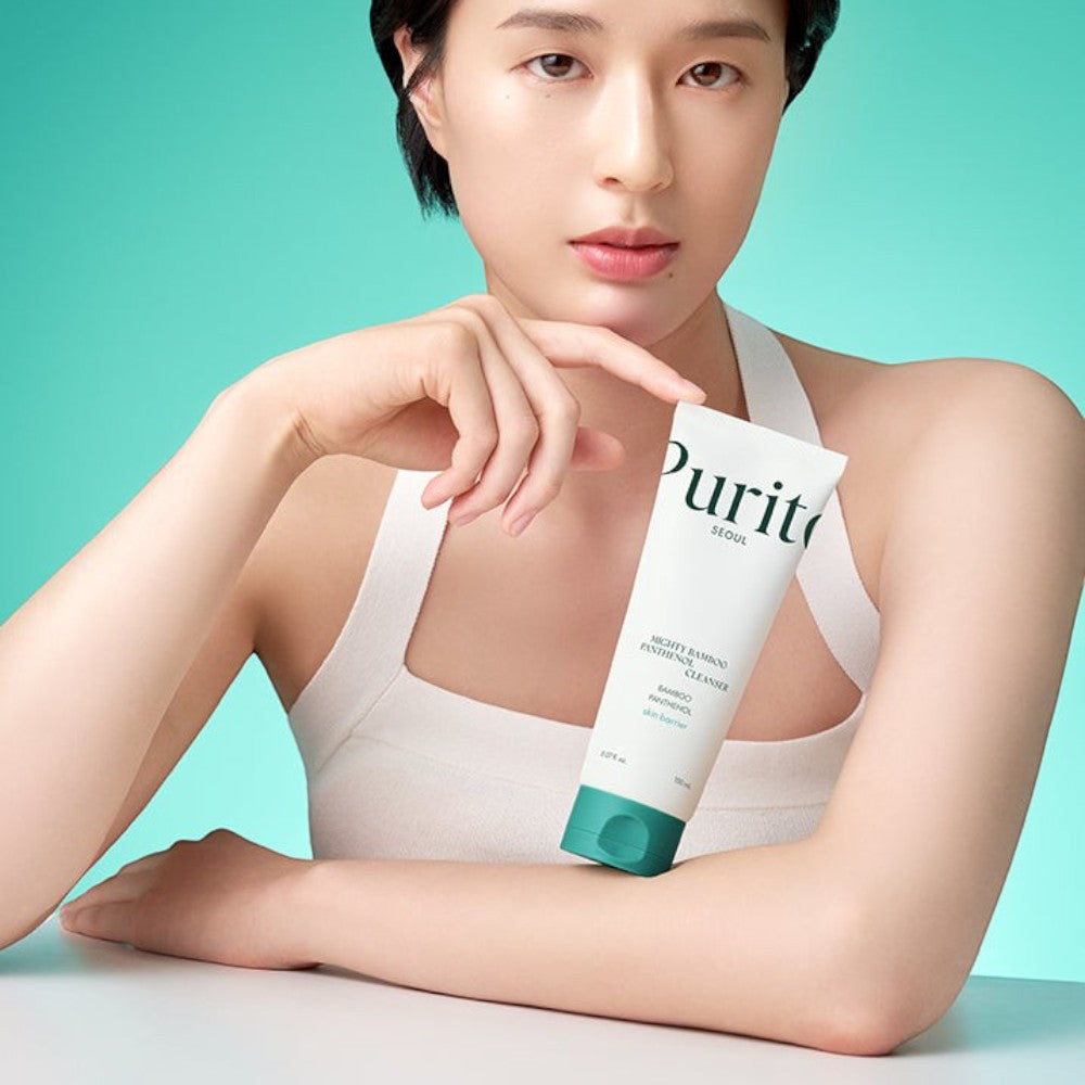 Skin TOGO model holding a white tube of Purito Mighty Bamboo Panthenol Cleanser against a soft green background.