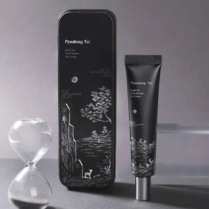 Skin TOGO Pyunkang Yul Black Tea Time Reverse Eye Cream tube and decorative black tin with hourglass on grey background