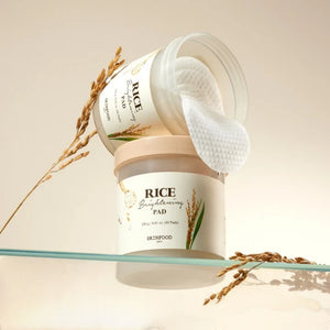 Skin TOGO SKINFOOD Rice Brightening Pads in a jar with textured cotton pads and rice stalks on a glass shelf.