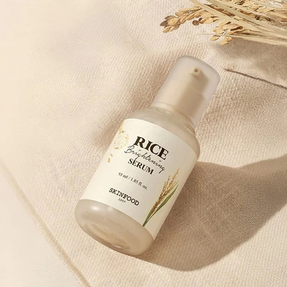 Skin TOGO SKINFOOD Rice Brightening Serum in a 55ml glass bottle with a pump dispenser on a beige fabric background.