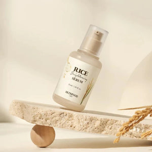 Skin TOGO SKINFOOD Rice Brightening Serum in a glass pump bottle balanced on a stone slab with dried rice stalks.