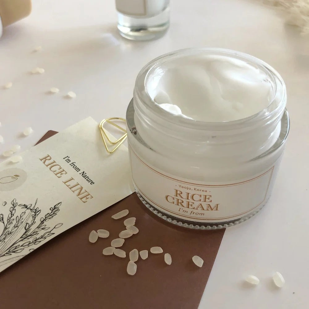 Skin TOGO I'm from Rice Cream in a glass jar with white nourishing texture, surrounded by rice grains on a table.