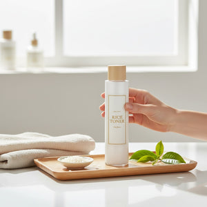 Skin TOGO I'm from Rice Toner bottle held by a hand on a wooden tray with rice grains and a green leaf
