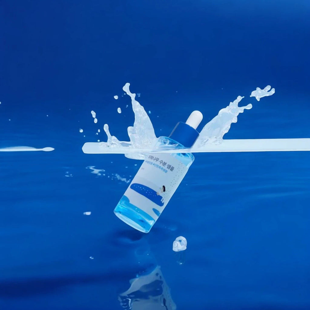 Skin TOGO Round Lab Birch Juice Moisturizing Ampoule bottle splashing in water against a vibrant blue background.