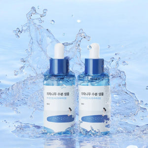 Skin TOGO Round Lab Birch Juice Moisturizing Ampoule bottles surrounded by a refreshing water splash effect.