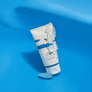Skin TOGO Round Lab Birch Juice Moisturizing Cleanser tube with creamy foam texture on a vibrant blue background.