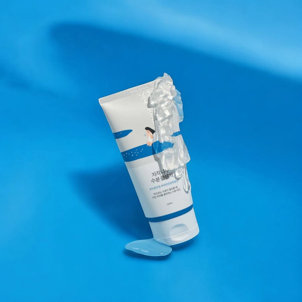 Skin TOGO Round Lab Birch Juice Moisturizing Cleanser tube with creamy foam texture on a vibrant blue background.