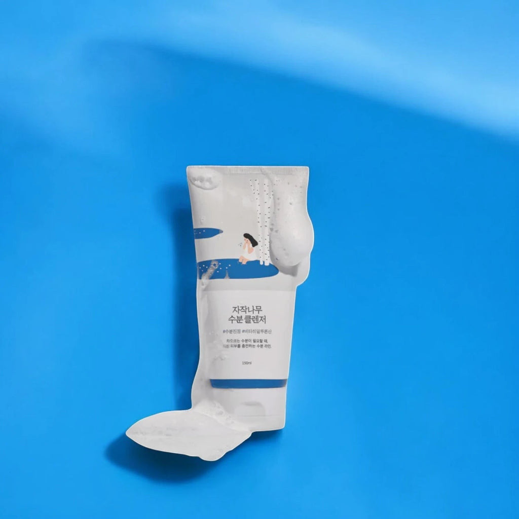 Skin TOGO Round Lab Birch Juice Moisturizing Cleanser tube with creamy foam on a vibrant blue background.