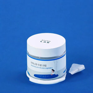 Skin TOGO Round Lab Birch Juice Moisturizing Cream in a white jar with blue accents on a vibrant blue background.