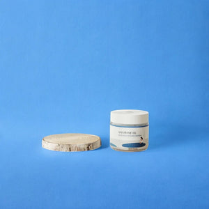 Skin TOGO Round Lab Birch Juice Moisturizing Cream in a glass jar next to a small wooden slice on a blue background