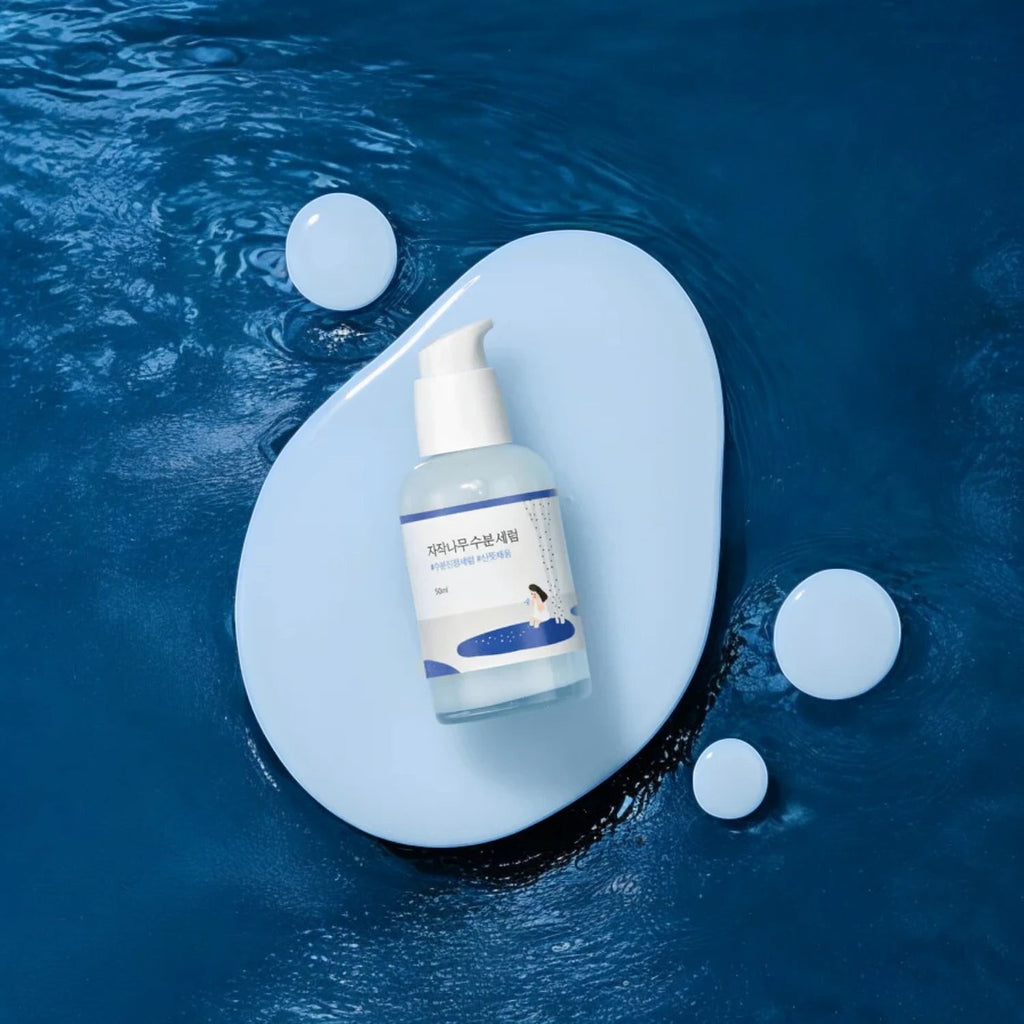 Skin TOGO Round Lab Birch Juice Moisturizing Serum bottle on a blue stone platform surrounded by water ripples.