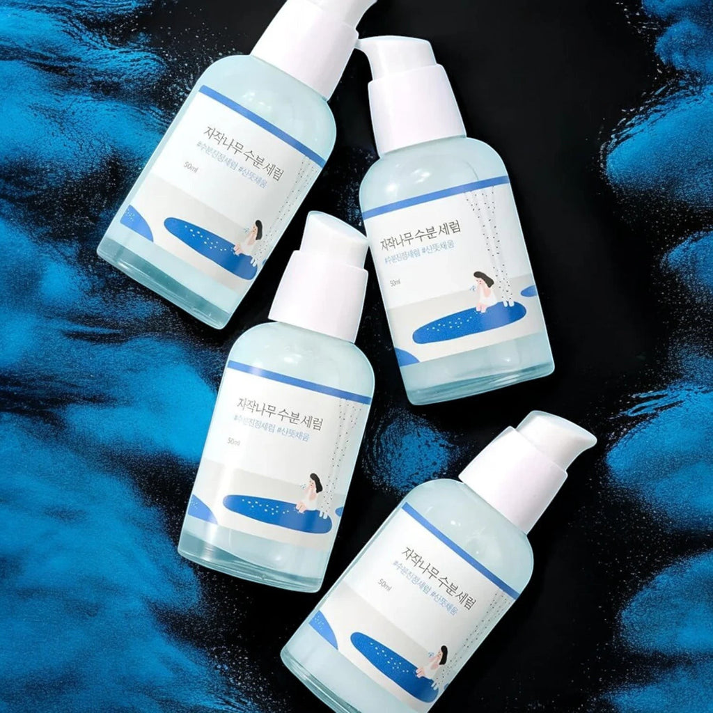 Skin TOGO Round Lab Birch Juice Moisturizing Serum bottles with light blue liquid on a dark blue textured background.