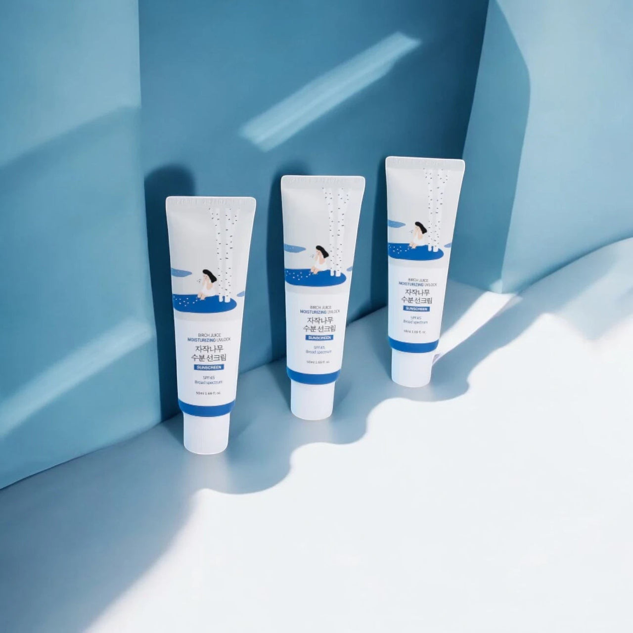 Skin TOGO Round Lab Birch Juice Moisturizing Sun Cream tubes with SPF 50+ PA++++ protection on a blue background.
