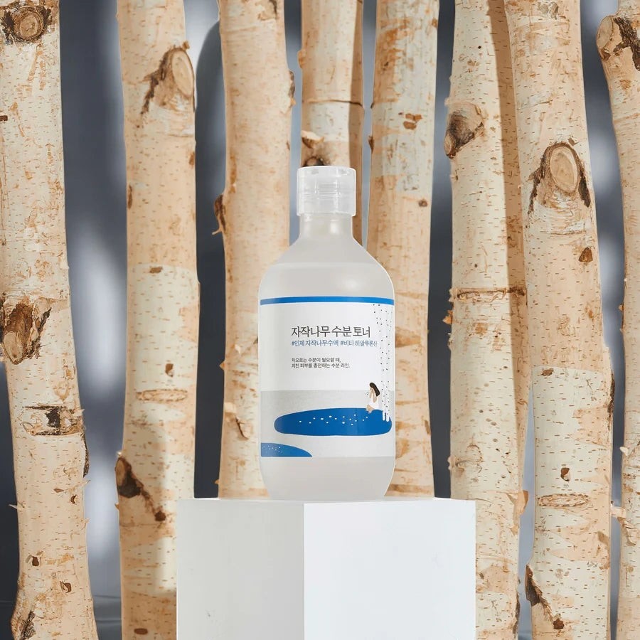 Skin TOGO Round Lab Birch Juice Moisturizing Toner bottle displayed on a white pedestal against birch tree trunks.