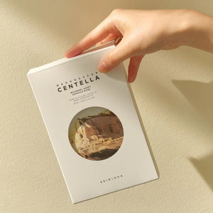 Skin TOGO hand holding a white SKIN1004 Madagascar Centella Watergel Sheet Ampoule Mask box against a beige wall