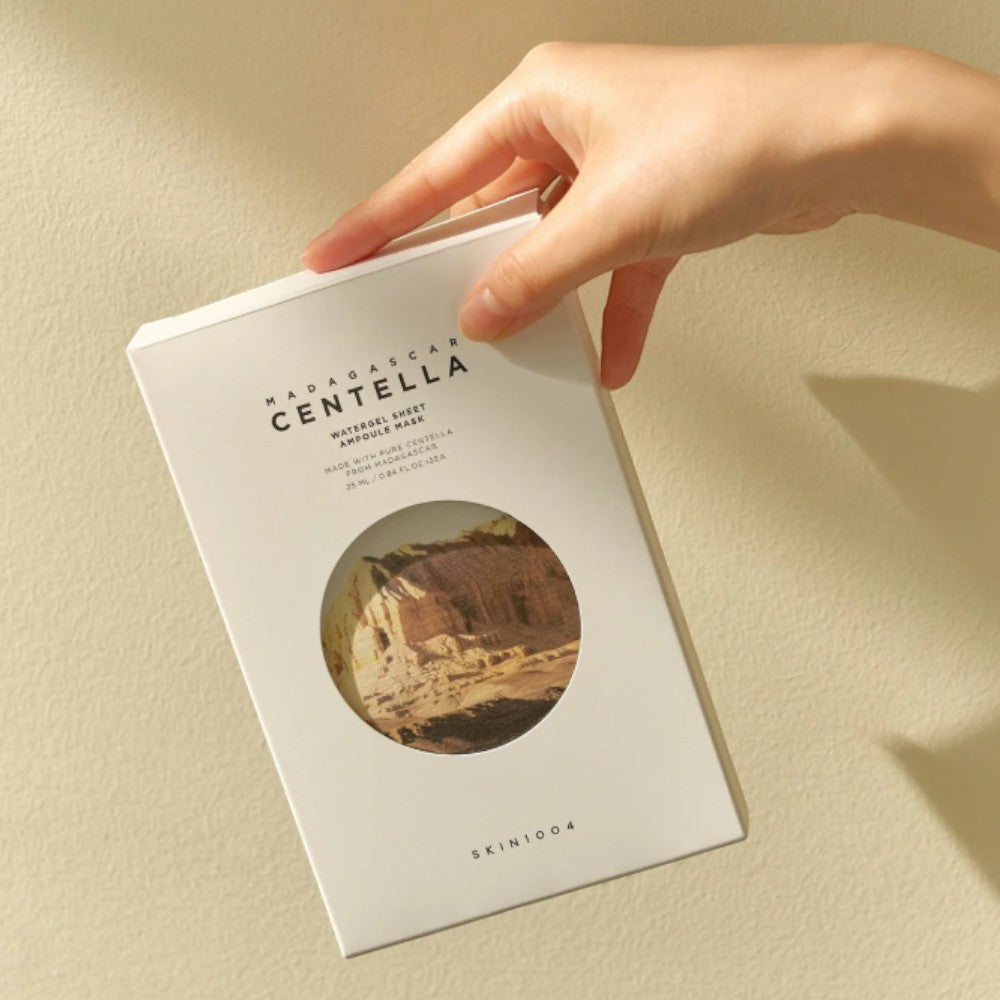 Skin TOGO hand holding a white SKIN1004 Madagascar Centella Watergel Sheet Ampoule Mask box against a beige wall