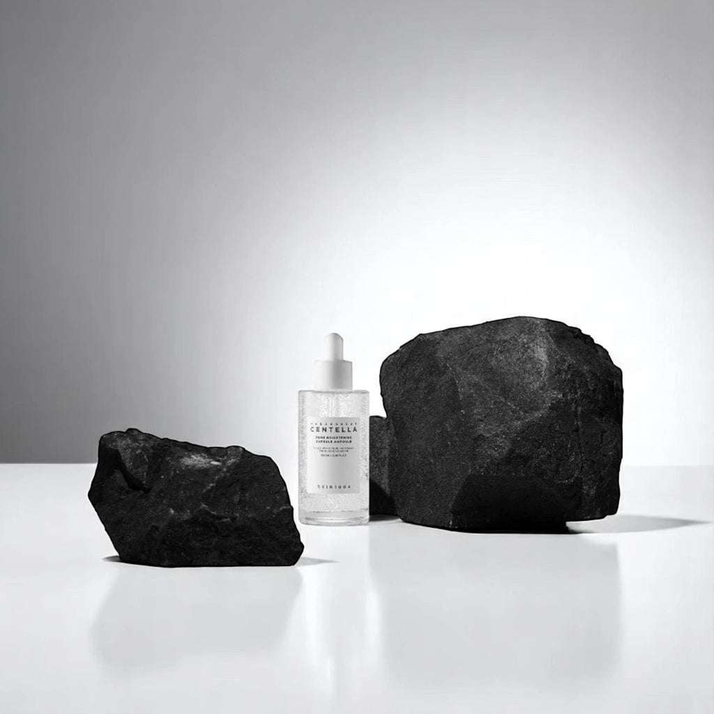 Skin TOGO SKIN1004 Centella Tone Capsule Ampoule bottle placed between two large black volcanic rocks on a white surface.