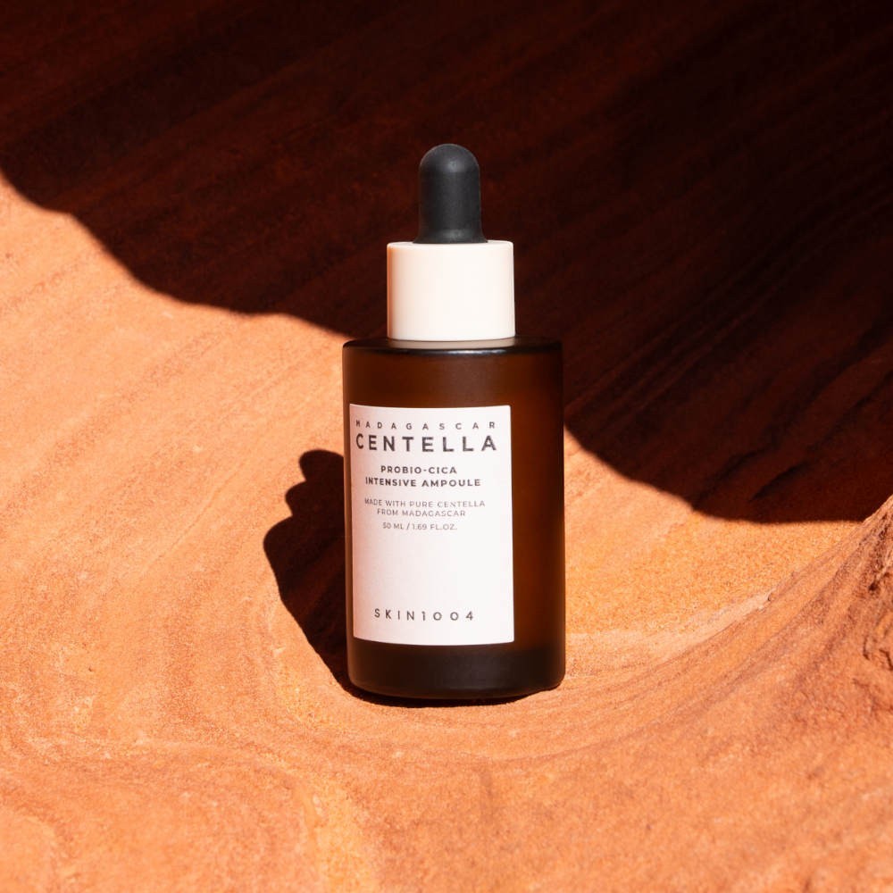 Skin TOGO SKIN1004 Madagascar Centella Probio-Cica Intensive Ampoule in a brown glass bottle on textured orange sand.