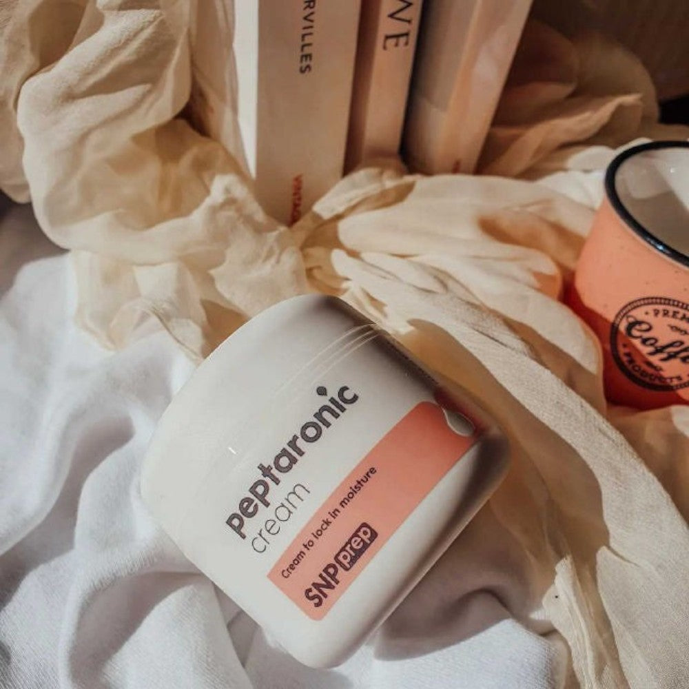 Skin TOGO SNP Prep Peptaronic anti-aging face cream in a white jar with pink label, set on soft fabric with books.