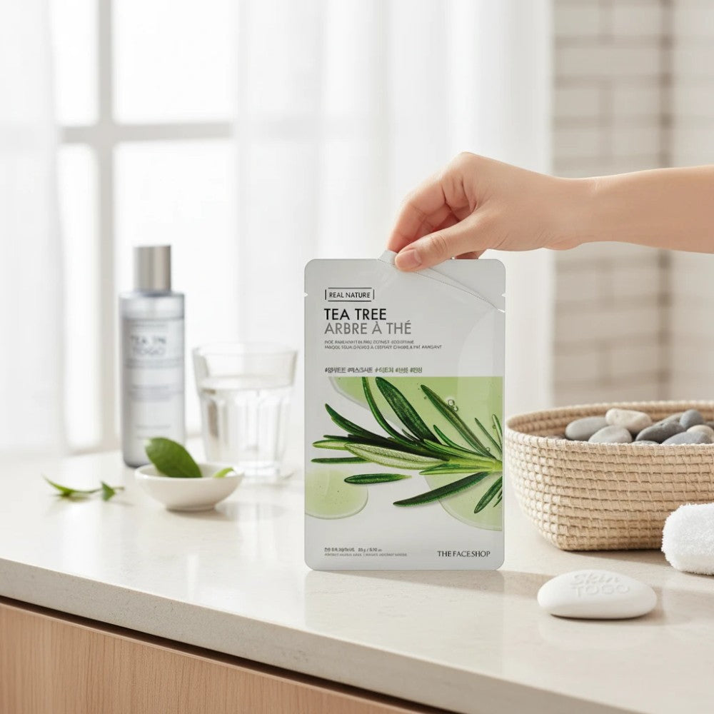 Skin TOGO The Face Shop Real Nature Tea Tree sheet mask held by a hand on a bright, minimalist bathroom counter.
