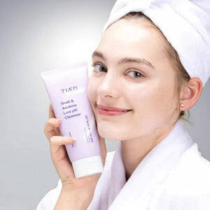 Skin TOGO model holding a TIAM Snail & Azulene Low pH Cleanser tube, wearing a white robe and hair towel.