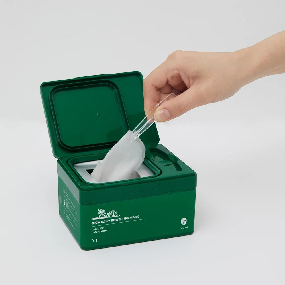 Skin TOGO VT CICA Daily Soothing Mask in a green dispenser box with a hand using tweezers to remove a sheet mask.