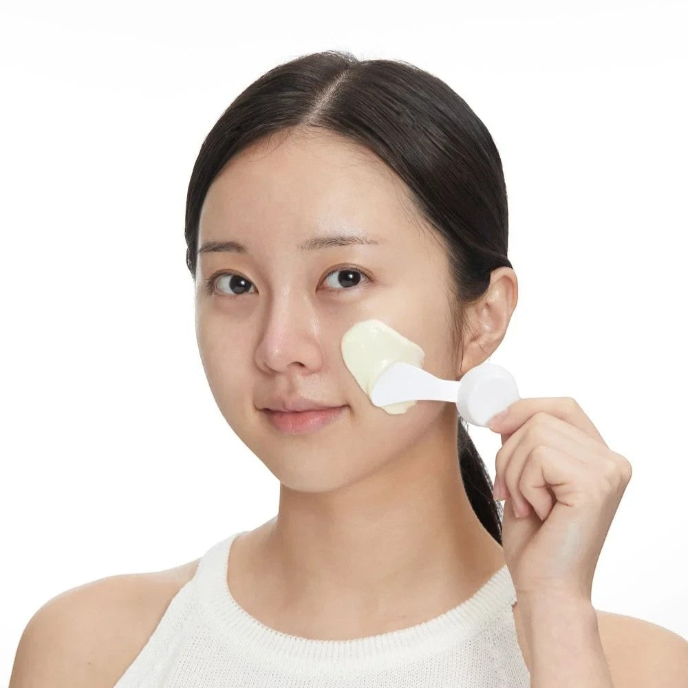 Skin TOGO model applying VT Cosmetics Reedle Shot Hyaluronic Modeling Pack with a white spatula to her cheek